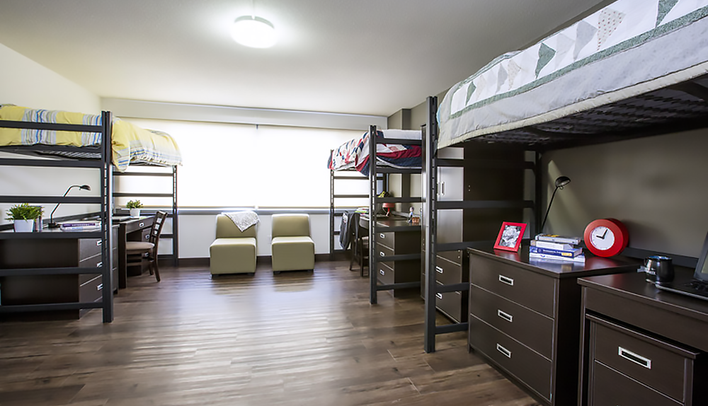 Room containing three modern loft beds with desks underneath, comfortable seating and hardwood floors.