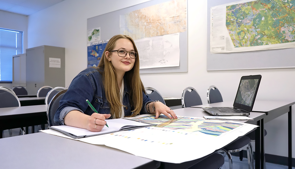 Student taking notes in a notebook while studying a large map.