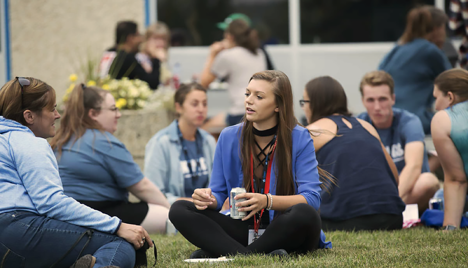 Students sitting and socializing in grassy area.