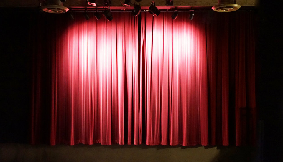 Bright lights and large red drapes on the stage at the front of the room